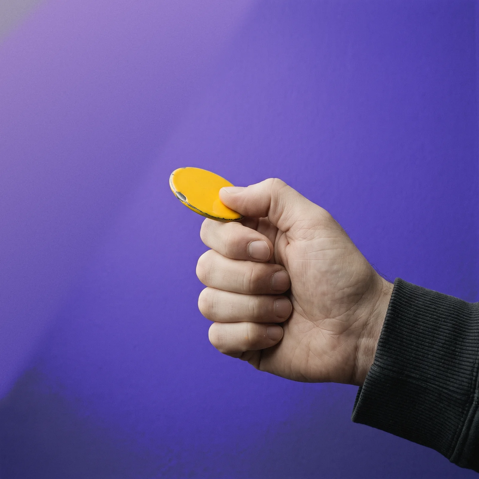 A yellow coin balanced on a thumb, ready to flick